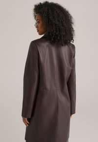 Abrigo de cuero marrón con un diseño a medida, corte recto y mangas largas. Textura suave, costuras visibles y un cuello alto.