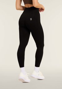 Leggings neri a vita alta con una texture liscia e un logo argento sul retro. Abbinati a scarpe sportive bianche e calzini corti.