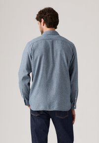Blue, textured shirt with long sleeves and a pointed collar. Features buttoned cuffs and a subtle pattern. Worn with dark jeans.