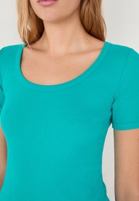 Turquoise geribbelde aansluitende top met een ronde halslijn en korte mouwen, gemaakt van rekbare stof, met een gladde textuur.