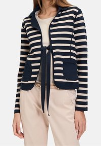 Randig cardigan i marinblått och krämfärgat, med en knytning som stängning, dubbla framfickor, mjukt tyg och utan krage.