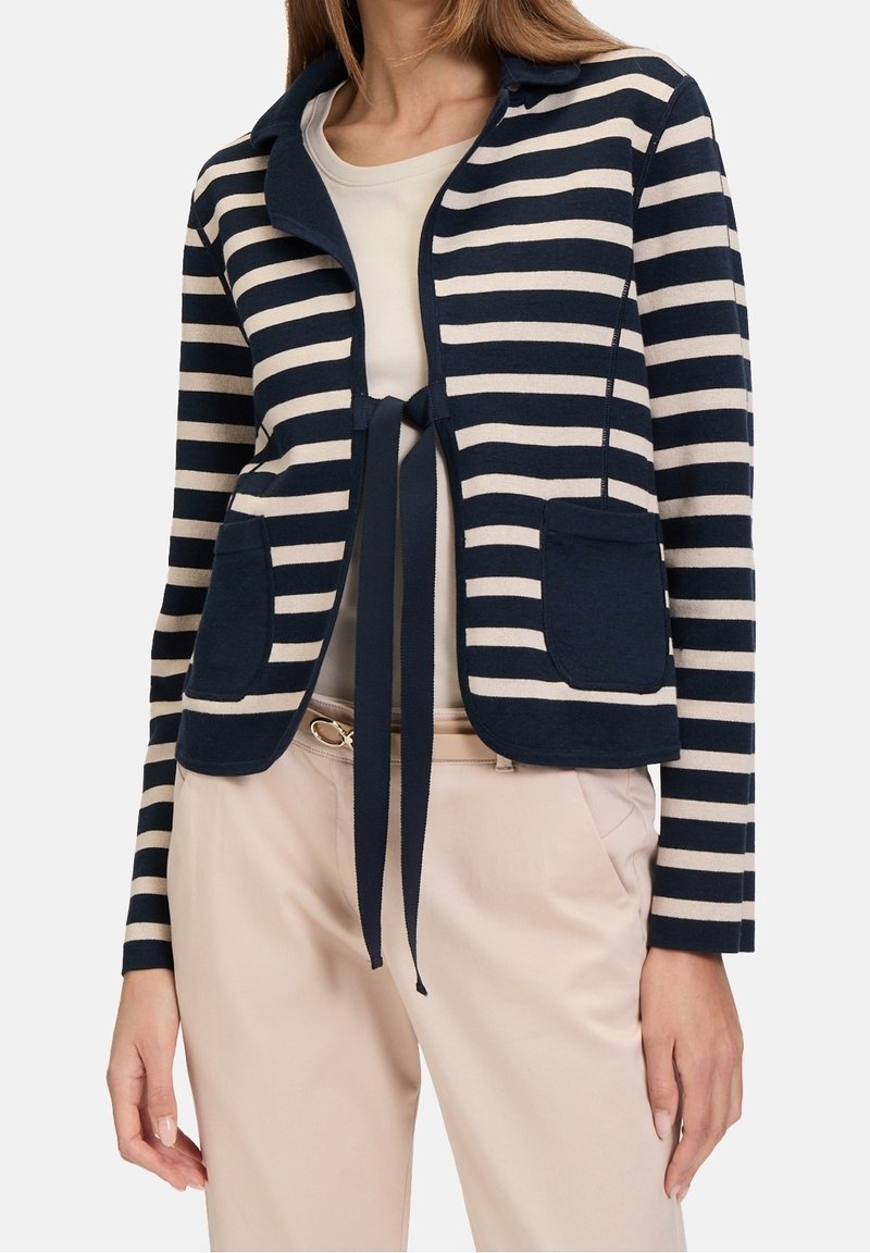 Randig cardigan i marinblått och krämfärgat, med en knytning som stängning, dubbla framfickor, mjukt tyg och utan krage.