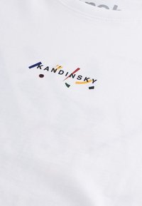Valkoinen puuvillainen t-paita, jossa on monivärinen teksti "KANDINSKY" leikkisässä asettelussa, jossa on erilaisia muotoja ja korosteita.
