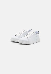 Baskets en cuir blanc avec des lacets plats, des bouts arrondis et de subtiles perforations. Elles présentent un accent texturé au talon et un design minimaliste.