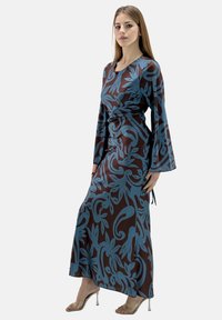 Robe longue marron avec des motifs floraux bleus, dotée de longues manches évasées et d'une taille nouée. Fabriquée en tissu lisse, elle présente une silhouette fluide.