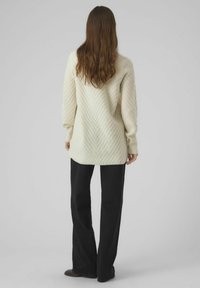 Cream-colored knitted sweater with a chevron pattern, ribbed cuffs, and a relaxed fit, paired with black flared pants.