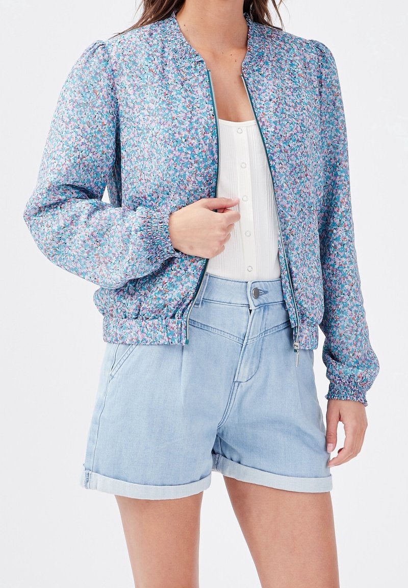 Bomberjack met bloemenprint in blauw- en roze tinten, met geplooide mouwen en een aansluitende taille. Gecombineerd met lichte denim shorts.