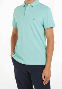 Polo in cotone turchese chiaro con colletto a tre bottoni, maniche corte e un piccolo logo sul petto. Abbinato a pantaloni blu navy.