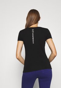 T-shirt noir à manches courtes avec un design ajusté, comportant une impression de logo blanc vertical au dos. Tissu lisse et encolure ronde.