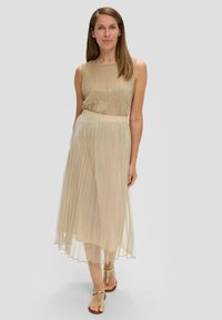 Robe dorée légère avec une jupe plissée, un haut sans manches et un corsage texturé. Associée à des sandales dorées, l'apparence est élégante et fluide.