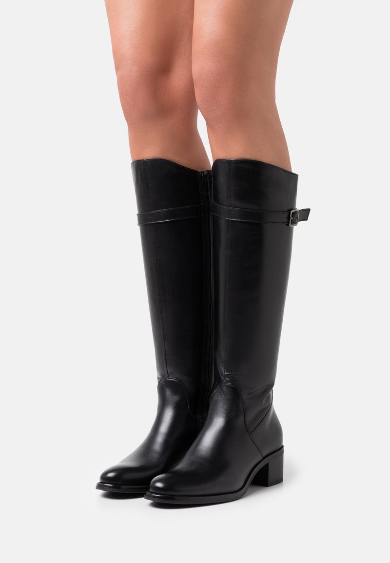 Schwarze kniehohe Stiefel aus Leder mit glatter Textur, Blockabsatz, seitlichem Reißverschluss und verstellbarem Riemendetail am oberen Ende.