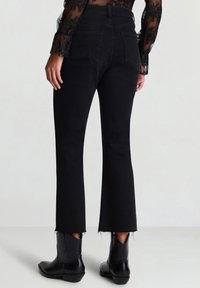 Jeans neri svasati con orlo grezzo, vita alta e tasche posteriori. Abbinati a stivaletti neri, il tessuto ha una texture liscia.