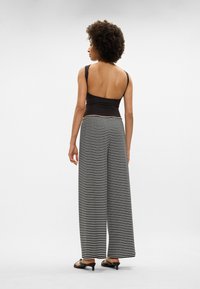 Top preto sem mangas combinado com calças largas de riscas pretas e brancas; tecido suave com um ajuste descontraído e uma cintura alta.