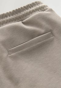 Pantalons de survêtement beige clair avec une texture douce, dotés d'une taille élastique et d'une petite poche arrière rectangulaire.