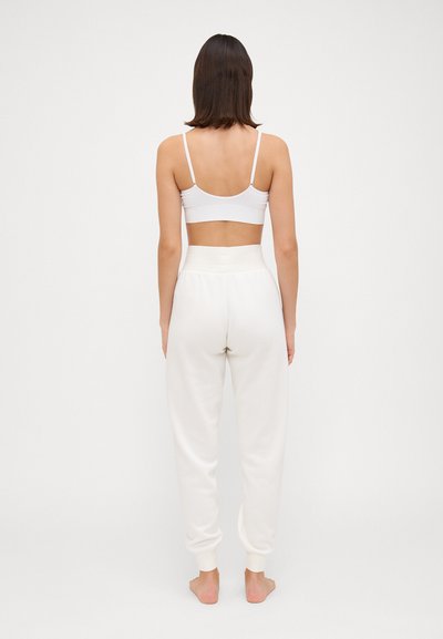 Reggiseno sportivo bianco e pantaloni jogger crema realizzati in materiale morbido, con vita alta e polsini affusolati. Dettagli di cuciture visibili.