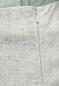 Κοντινό πλάνο γκρι υφασμάτινης φούστας με λευκό φερμουάρ στο πίσω μέρος, συνδυασμένη με ανοιχτοπράσινο πλεκτό τοπ.