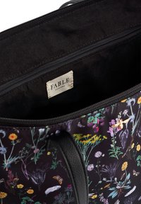 Black floral tote bag with vibrant multicolored flowers, including yellow and purple, and a black interior. Zippered closure and fabric tag visible.