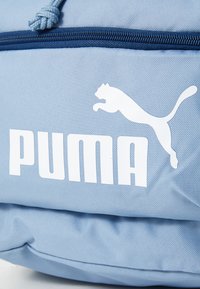 Light blue sports bag with white "PUMA" logo. Made from textured fabric, featuring a zip closure and a raised, leaping puma graphic.