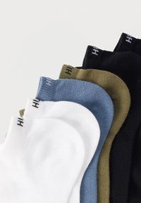 Πέντε ζεύγη κάλτσες σε λευκό, ανοιχτό μπλε, ελιά και μαύρο. Κάθε ζευγάρι έχει ριμπ υφή και ένα λογότυπο στη μανσέτα.