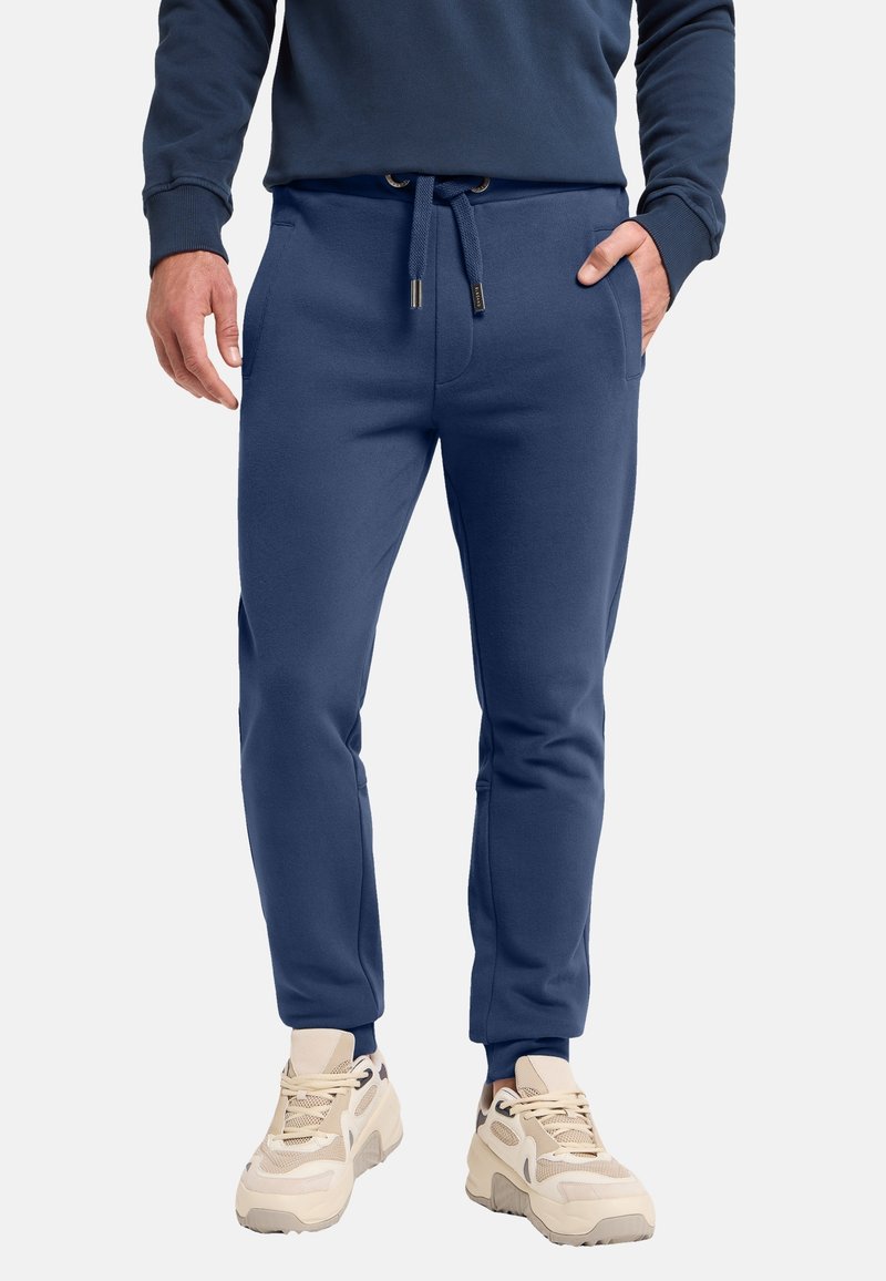 Marineblaue Jogginghosen aus weichem Stoff mit elastischem Bund, Kordelzug, seitlichen Taschen und schmal zulaufenden Säumen, getragen mit hellen Sneakers.