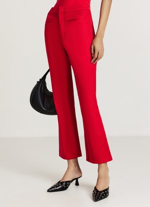 Pantalon rouge taille haute avec un devant plat, jambes larges et poches latérales. Associé à des mules noires à bout pointu avec des accents argentés.
