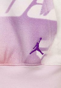 Un tejido atlético con un degradado púrpura y rosa presenta un diseño texturizado, con un destacado logo de Jumpman púrpura bordado cerca de la costura.
