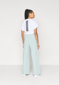 Vit t-shirt med svarta vertikala ränder på baksidan, kombinerad med ljusblå vida byxor. Har resår i midjan och mjukt tyg.