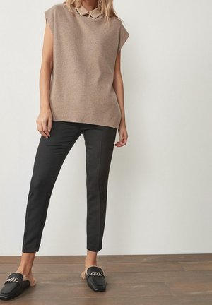 Lichtbruine geribbelde trui met kraag, gecombineerd met zwarte slim-fit broek. Zwarte instapschoenen met bontaccent en kettingdetail.