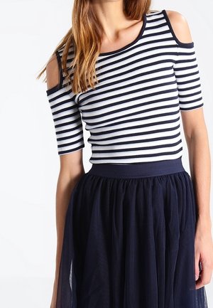 Femme portant un top à épaules dénudées rayé noir et blanc associé à une jupe en tulle bleu marine foncé.