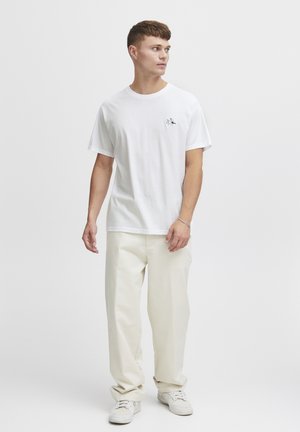 Hvid bomulds t-shirt med korte ærmer og rund halsudskæring, der har et lille, farverigt broderet design på venstre bryst. Sæt den sammen med beige bukser.