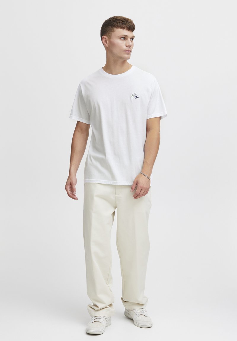 Hvid bomulds t-shirt med korte ærmer og rund halsudskæring, der har et lille, farverigt broderet design på venstre bryst. Sæt den sammen med beige bukser.
