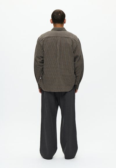 Kockás barna és fekete ing, gombos állással és felhajtott mandzsettákkal, laza szürke nadrággal párosítva. Texturált anyag.
