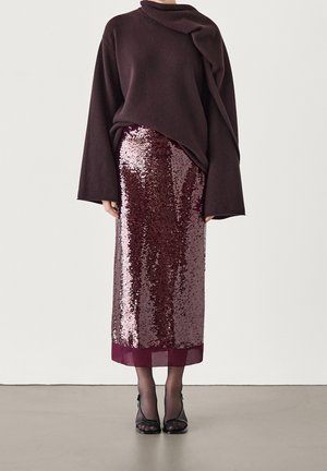 Fioletowy oversize'owy sweter z drapowanym dekoltem, zestawiony z bordową spódnicą z cekinami o długości do kolan, z mankietem wykonanym z jednolitego materiału.