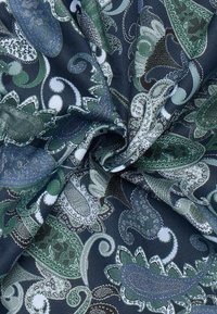 Navy stof met een paisleypatroon in groen, wit en metallic kleuren. De textuur is soepel met ingewikkelde details en krommingen.