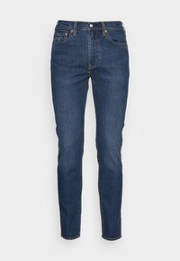 Jeans de mezclilla ajustados en azul oscuro con cierre de botón y cremallera, cinco bolsillos y costuras naranjas sobre un fondo blanco.