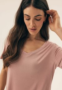 Jasnoróżowa koszulka typu V-neck wykonana z miękkiego materiału, z krótkimi rękawami i luźnym krojem, o gładkiej fakturze i subtelnym połysku.