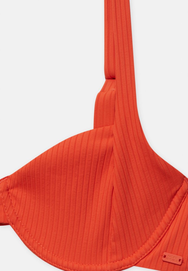 Orange ribbad bh med sömlösa kupor, justerbara band och en märkestämpel. Tyget verkar slätt med en matt finish.