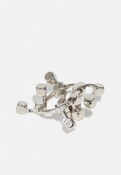 Bague en argent avec plusieurs petits accents géométriques, présentant une texture lisse et brillante ainsi que des formes cylindriques avec des sommets plats.