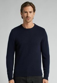 Suéter de punto azul marino con cuello redondo, mangas largas, puños y dobladillo acanalados. Fabricado con material suave y de textura lisa.