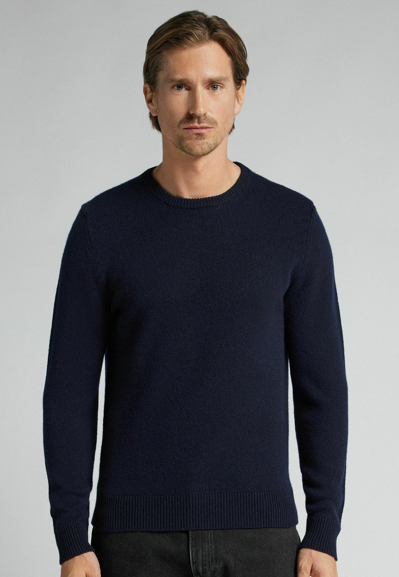 Suéter de punto azul marino con cuello redondo, mangas largas, puños y dobladillo acanalados. Fabricado con material suave y de textura lisa.