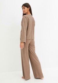 Ensemble de détente en maille marron avec une coupe décontractée. Haut à manches longues et pantalon large, présentant une texture douce et un design simple.