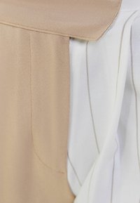 Tan- och vit skjorta som visar en texturerad tyg. Har en kragsdesign med subtila vertikala ränder på den vita sidan.