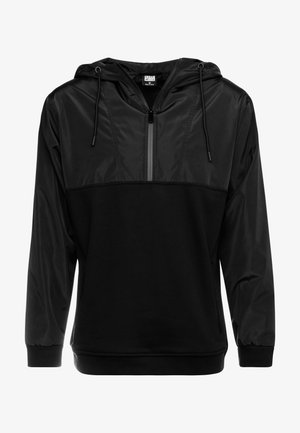 Svart pullover-jakke med glidelås foran, laget av kontrasterende matte og blanke materialer; har hette og elastiske ermer.