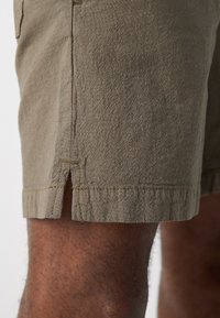 Khaki shorts med en tekstureret stof, der har en sideslids og kontrastsyninger. Sømmen er afsluttet med en simpel stikning.