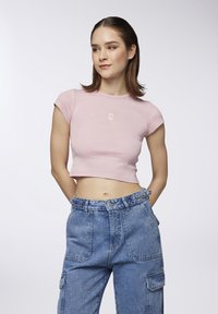 T-shirt cropped rosa con maniche corte e ricamo di un orso sul petto, abbinata a pantaloni cargo in denim blu a vita alta con tasche.