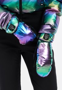 Regenboogkleurige geïsoleerde wanten met een gestikte textuur, voorzien van zwarte accenten en een merketiket, gedragen over zwarte broeken.