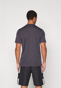 Camiseta de manga corta gris oscuro con una textura suave, cuello redondeado y un corte relajado. Llevada con pantalones cortos negros que cuentan con rayas blancas en los costados.