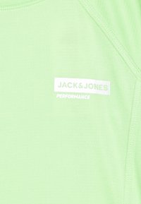 Světlezelené sportovní tričko s texturovanou tkaninou, raglánovými rukávy a bílou nášivkou s nápisem "JACK & JONES" a "PERFORMANCE."