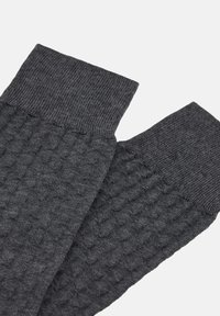 Guanti grigi con texture, dotati di polsino a costine e superficie decorata. Il materiale sembra morbido e lavorato a maglia, caratterizzato da un design a nido d'ape.