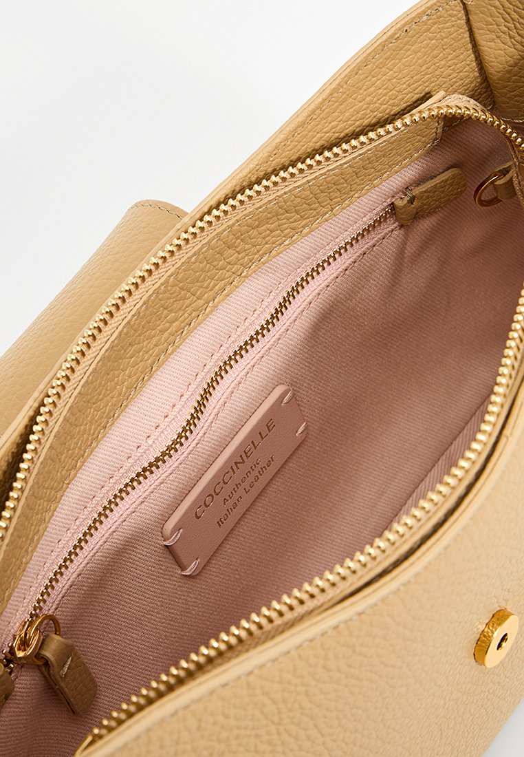Innenraum einer handgefertigten, tan-farbenen Ledertasche mit pinkem Stofffutter, goldfarbenem Reißverschluss und einem Etikett mit der Aufschrift "Coccinelle Authentisches italienisches Leder."